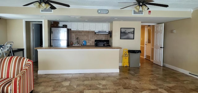 kitchen featuring crown molding, decorative backsplash, stove, freestanding refrigerator, and under cabinet range hood