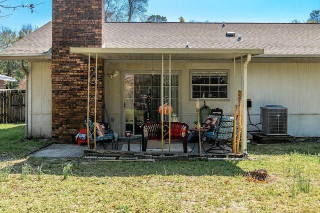 rear view of property featuring a patio, central AC, a yard, a shingled roof, and a chimney