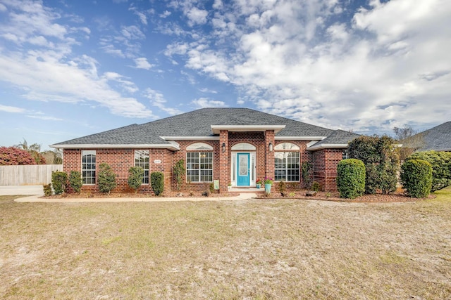 view of front of property with brick siding, roof with shingles, a front yard, and fence