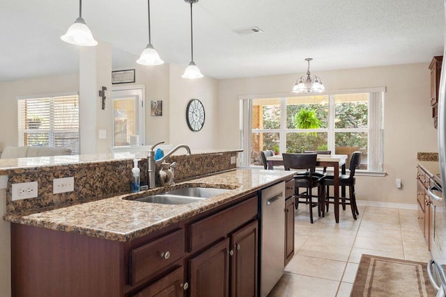 kitchen with decorative light fixtures, light tile patterned floors, stainless steel dishwasher, a sink, and light stone countertops