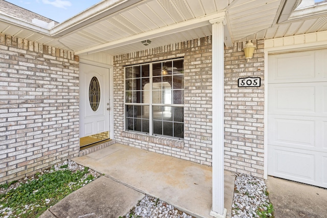 doorway to property featuring a garage, brick siding, and a porch