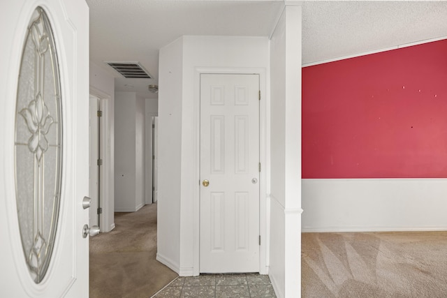 hallway featuring baseboards, carpet flooring, visible vents, and a textured ceiling