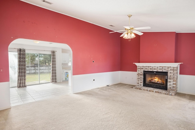 unfurnished living room with carpet, arched walkways, a brick fireplace, ceiling fan, and tile patterned floors