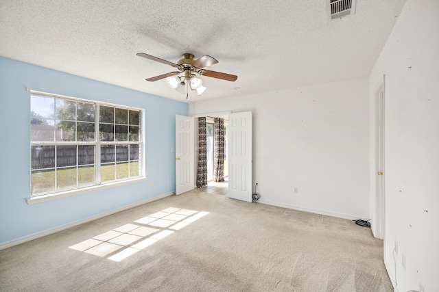 carpeted empty room featuring a ceiling fan, visible vents, a textured ceiling, and baseboards