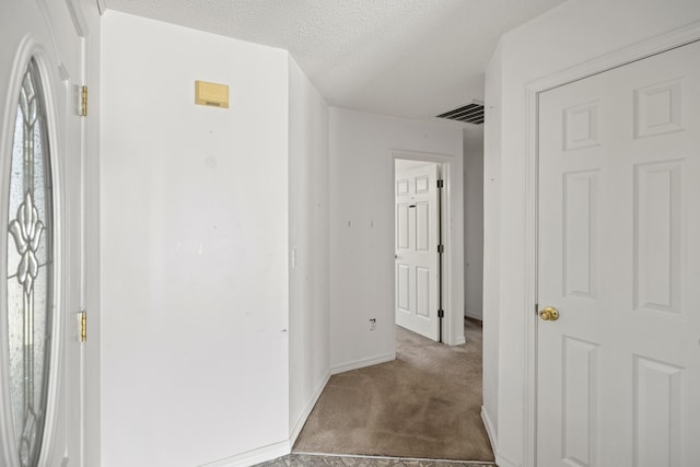 corridor with carpet, visible vents, a textured ceiling, and baseboards