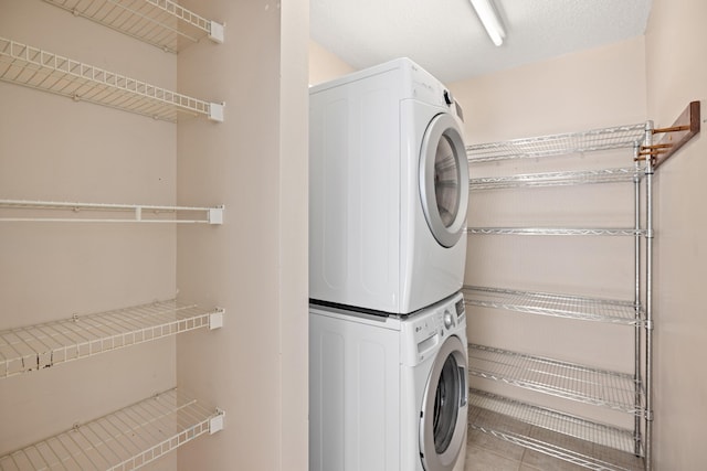 clothes washing area featuring stacked washer and dryer, tile patterned flooring, and laundry area