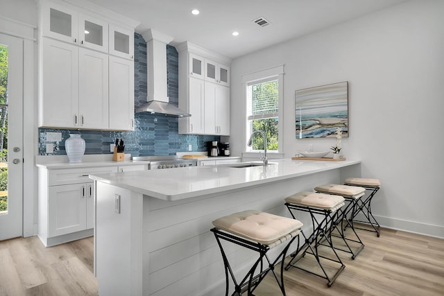 kitchen featuring light countertops, visible vents, backsplash, a sink, and wall chimney exhaust hood