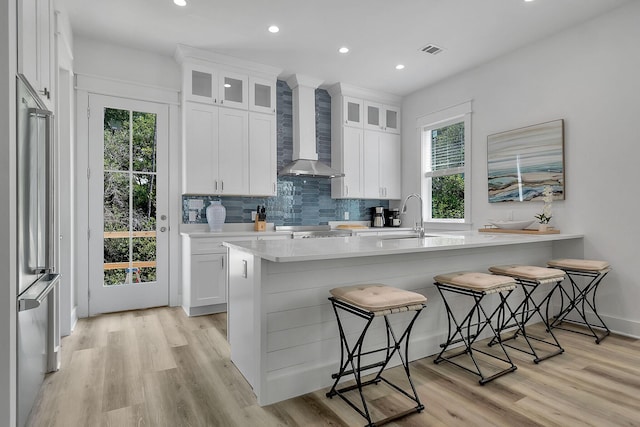 kitchen with wall chimney exhaust hood, visible vents, decorative backsplash, a sink, and a kitchen bar