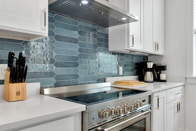 kitchen featuring wall chimney range hood, tasteful backsplash, white cabinetry, and high end range