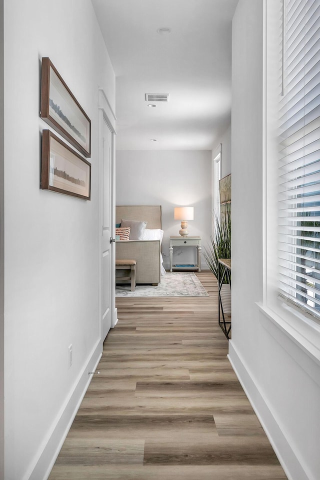 hall featuring baseboards, visible vents, a wealth of natural light, and wood finished floors