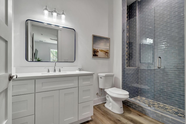 bathroom with a stall shower, baseboards, toilet, wood finished floors, and vanity