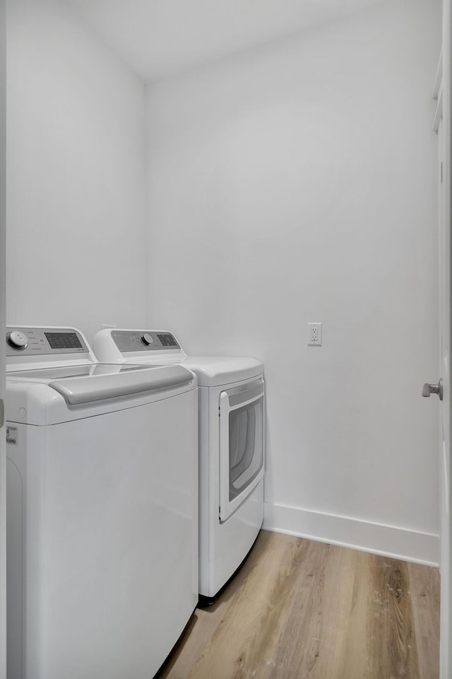 clothes washing area featuring laundry area, separate washer and dryer, light wood-style flooring, and baseboards