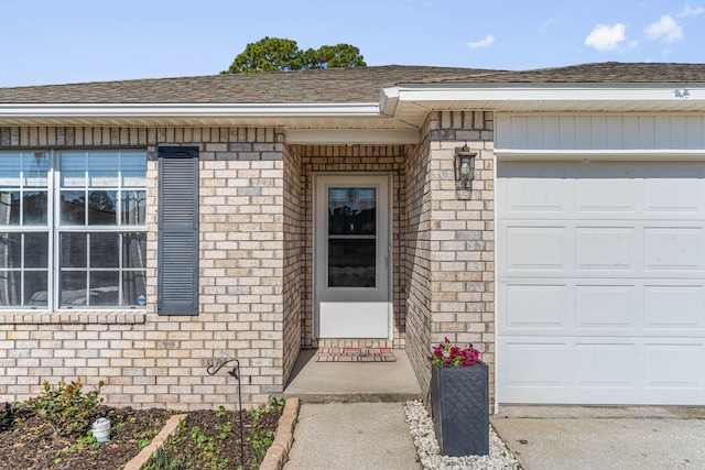 entrance to property featuring a garage, roof with shingles, and brick siding