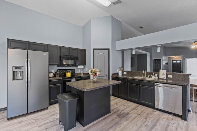 kitchen featuring light wood-style floors, dark countertops, a center island, black appliances, and a sink