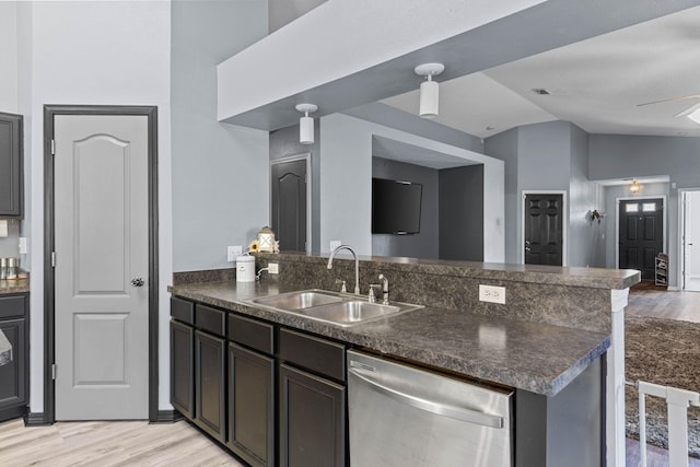 kitchen with light wood-type flooring, dark countertops, dishwasher, and a sink