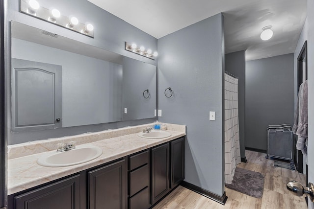 bathroom with double vanity, a sink, baseboards, and wood finished floors