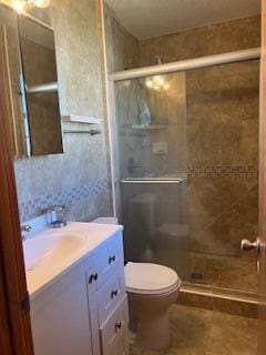 full bathroom featuring a stall shower, vanity, and toilet