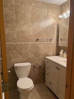 half bath with tile walls, vanity, toilet, and tile patterned floors