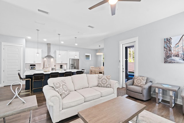 living area with baseboards, visible vents, ceiling fan, and dark wood-type flooring