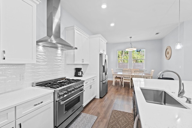 kitchen with stainless steel appliances, wood finished floors, a sink, light countertops, and wall chimney exhaust hood