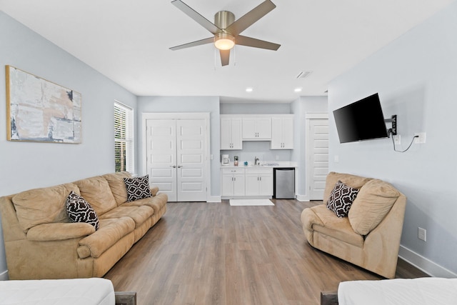 living area featuring indoor wet bar, light wood finished floors, visible vents, a ceiling fan, and baseboards