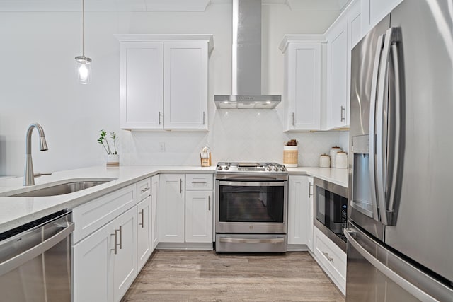 kitchen featuring light wood finished floors, wall chimney exhaust hood, appliances with stainless steel finishes, white cabinetry, and a sink