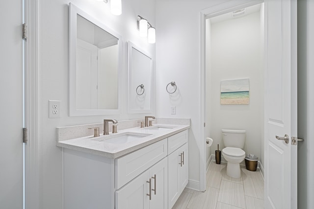 bathroom featuring baseboards, a sink, toilet, and double vanity