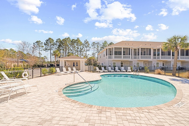 pool with a patio area, fence, and an outbuilding