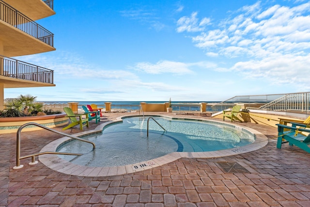 view of pool featuring a water view, a patio area, and a hot tub