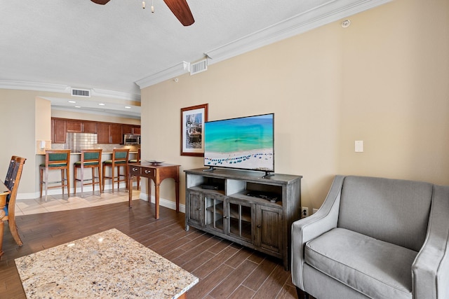 living area featuring dark wood-style floors, visible vents, crown molding, and ceiling fan