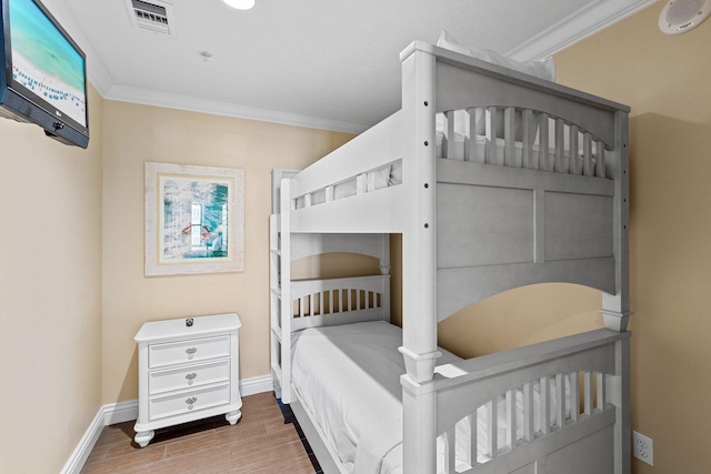 bedroom featuring visible vents, crown molding, baseboards, and wood finished floors