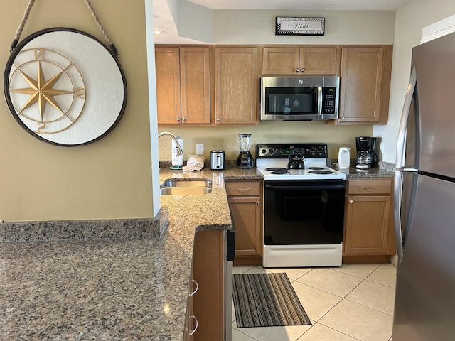 kitchen with light tile patterned floors, stone counters, stainless steel appliances, a sink, and brown cabinetry