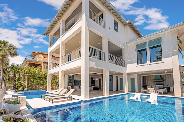 back of property featuring a patio, a balcony, an outdoor hangout area, stucco siding, and an infinity pool