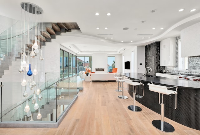 interior space with dark countertops, light wood-style flooring, a sink, white cabinetry, and backsplash