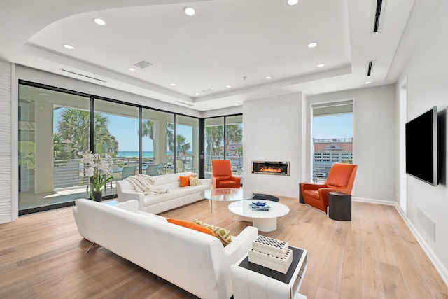 living room with a large fireplace, baseboards, light wood-style flooring, a tray ceiling, and recessed lighting