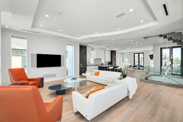 living room featuring light wood-style flooring, visible vents, a raised ceiling, and recessed lighting