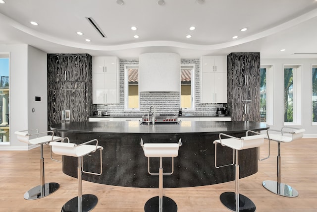 kitchen featuring tasteful backsplash, white cabinetry, a sink, and a kitchen bar