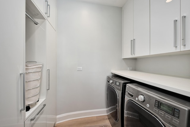 clothes washing area featuring cabinet space, light wood-style flooring, baseboards, and washer and dryer