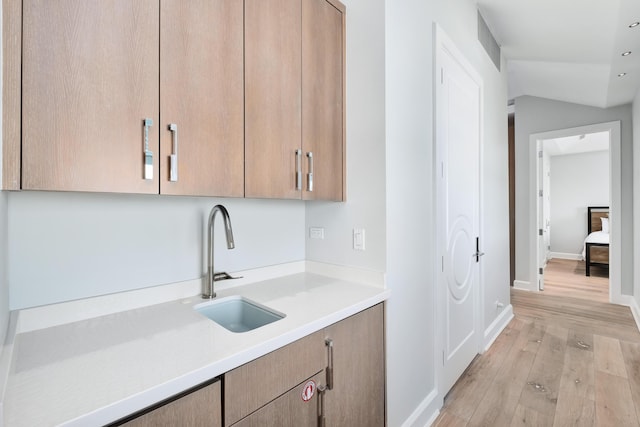 kitchen featuring baseboards, lofted ceiling, light wood-style flooring, light countertops, and a sink