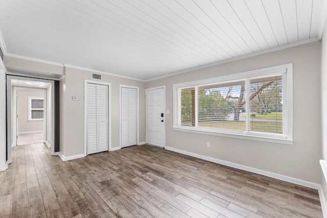 unfurnished bedroom featuring ornamental molding, wood finished floors, visible vents, and multiple closets