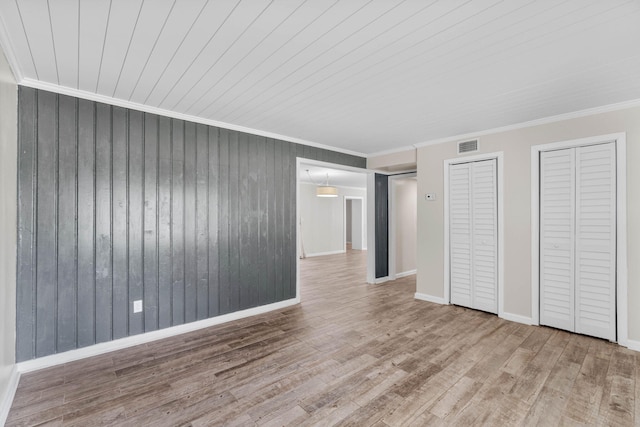 unfurnished bedroom with wood walls, wood finished floors, visible vents, two closets, and crown molding