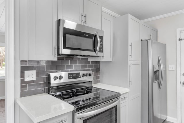 kitchen featuring white cabinets, light countertops, appliances with stainless steel finishes, backsplash, and crown molding