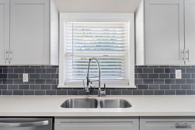 kitchen with decorative backsplash, stainless steel dishwasher, white cabinetry, a sink, and light stone countertops