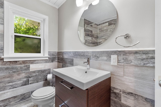 bathroom with tile walls, toilet, ornamental molding, wainscoting, and vanity