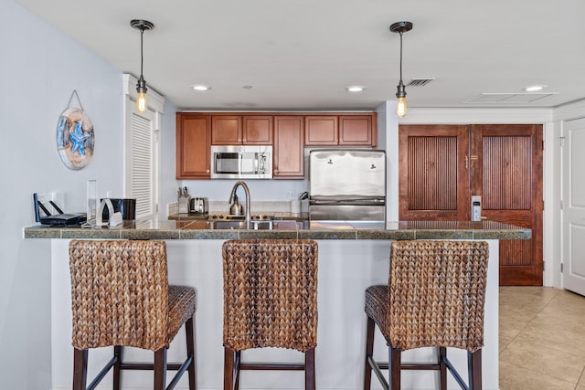 kitchen featuring stainless steel appliances, decorative light fixtures, tile countertops, and a kitchen breakfast bar