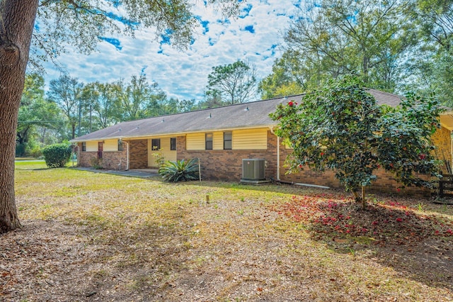 rear view of house featuring central AC, a yard, and brick siding