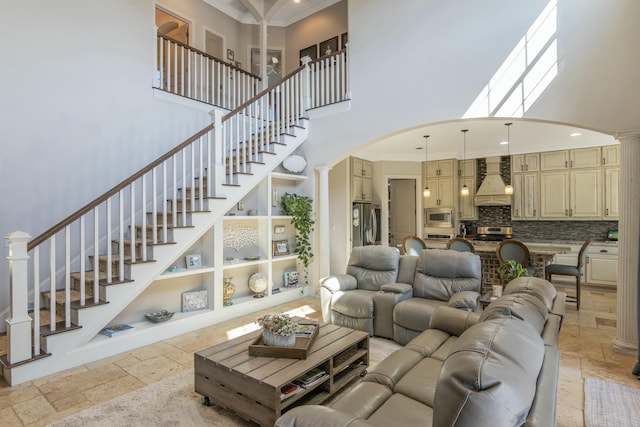 living area with ornate columns, stone tile floors, a high ceiling, and crown molding