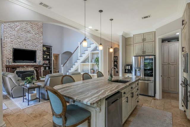 kitchen featuring stainless steel appliances, cream cabinetry, a sink, and stone tile floors