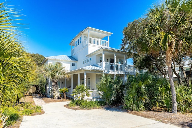 coastal home featuring a porch, concrete driveway, a standing seam roof, metal roof, and a balcony