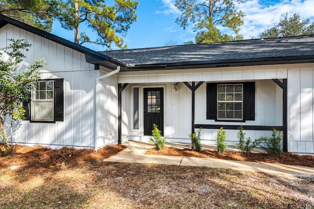 doorway to property featuring board and batten siding, covered porch, and roof with shingles